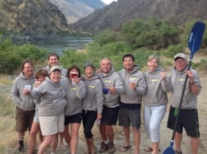 a group in gray sweatshirts poses during a whitewater rafting trip in from of a hells canyon vista