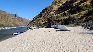 Four tents are set up on a Snake River beach in Hells Canyon