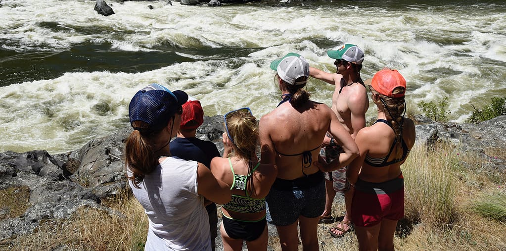 A guide points to a big rapid in Hells Canyon while a group listens