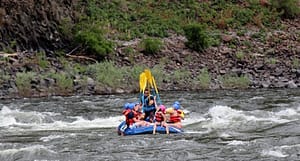 a raft full of rafters hold their paddles up high to celebrate going through a great rapid in hells canyon