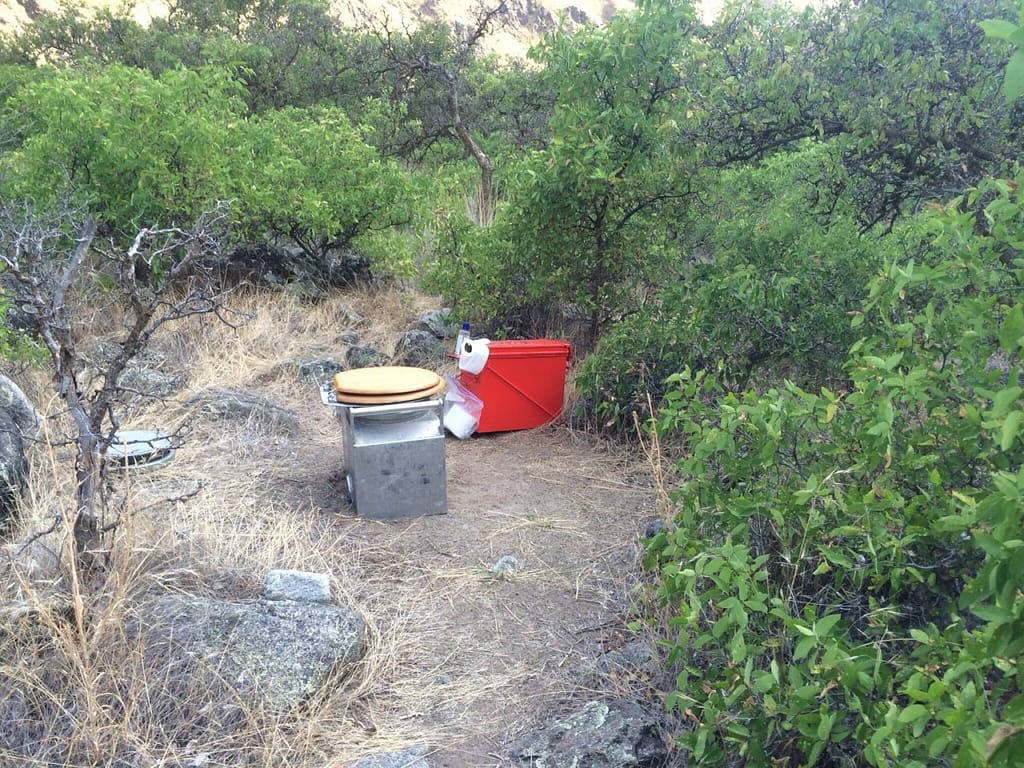 a river toilet called a groover tucked away in bushes on a multiday rafting trip in hells canyon