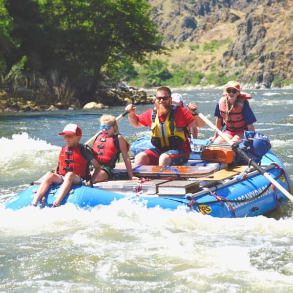 a group of kids on a raft smile and laugh while whitewater rafting in hells canyon