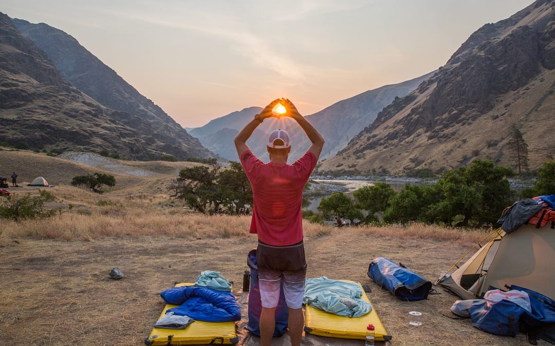 summer sun rises in hells canyon behind man holding his hands up to frame it