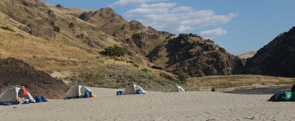 Tents are spread out on a sandy beach on the banks of the Salmon River, waiting fro the rafting trip to arrive