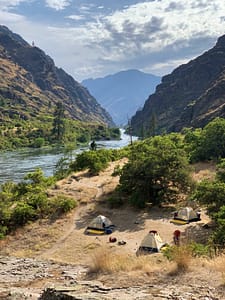 tents are set up riverside along the snake river during a hells canyon rafting trip