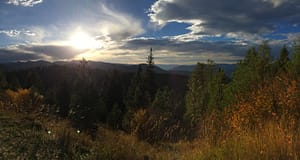 scenic mountain vista in idaho during the fall: blue sky and clouds, green pine, orange trees, dusk
