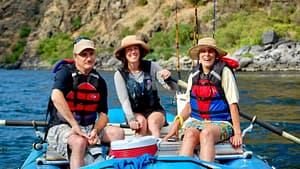 Three people smile while floating down the snake river on a whitewater rafting trip