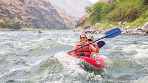 a girl smiles as she paddles an inflatable kayak through rapids on a snake river overnight rafting trip
