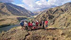 a large group stand on a ledge called suicide point overlooking the snake river and hells canyon