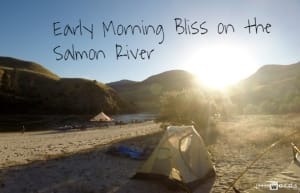 the sun rises over mountains and onto the salmon river beach, camp and tents on the whitewater rafting vacation. Written on the picture: early morning bliss on the salmon river