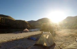 the sun rises above the mountains of the salmon river onto tents on the sandy beach on a multi day rafting trip