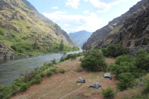 the snake river with tents on a grassy meadow and a great view of the deep walls in hells canyon on the snake river