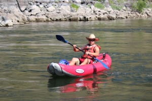 a man in a cowboy hat is in a red duckie or inflatable kayak on a overnight whitewater rafting trip