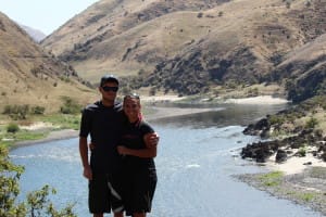 a couple poses in front of a scenic salmon river with sandy beaches and tall grassy banks during a rafting trip
