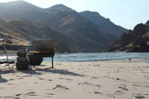 a river grill and stacked dutch ovens are cooking a delicious from scratch dinner on a sandy beach on a Salmon River rafting trip