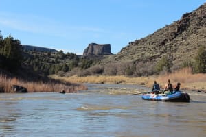 a boat floats down the owyhee river toward the surround lava rock formations on a multi day river trip