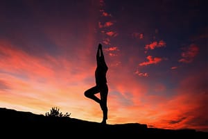 a woman does yoga riverside during a beautiful red and orange sunset