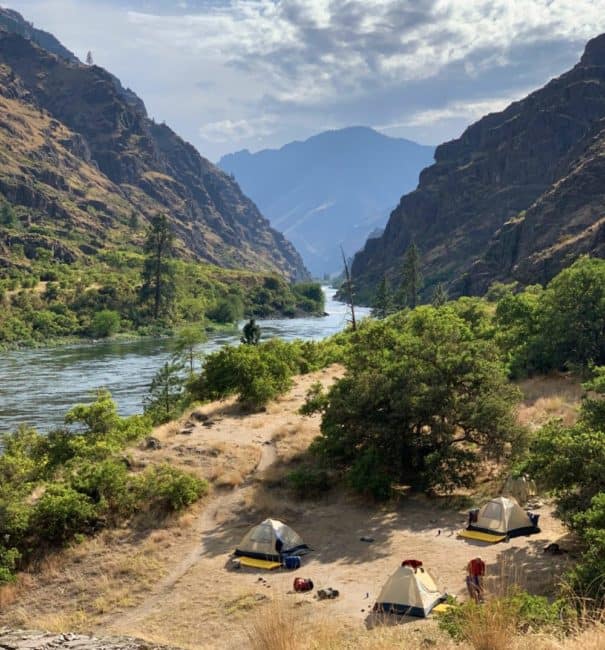 tents sit riverside with hells canyon and the snake river in the background
